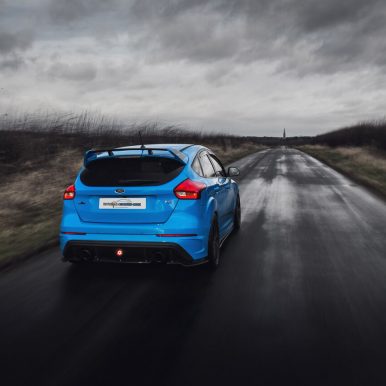 The image shows a blue Ford Focus RS MK3 dirivinf down a country road during stormy weather.