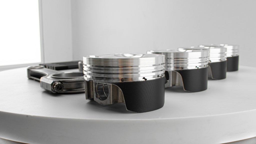 The Image shows a white photo studio background with a series of four Wossner piston heads in the foreground